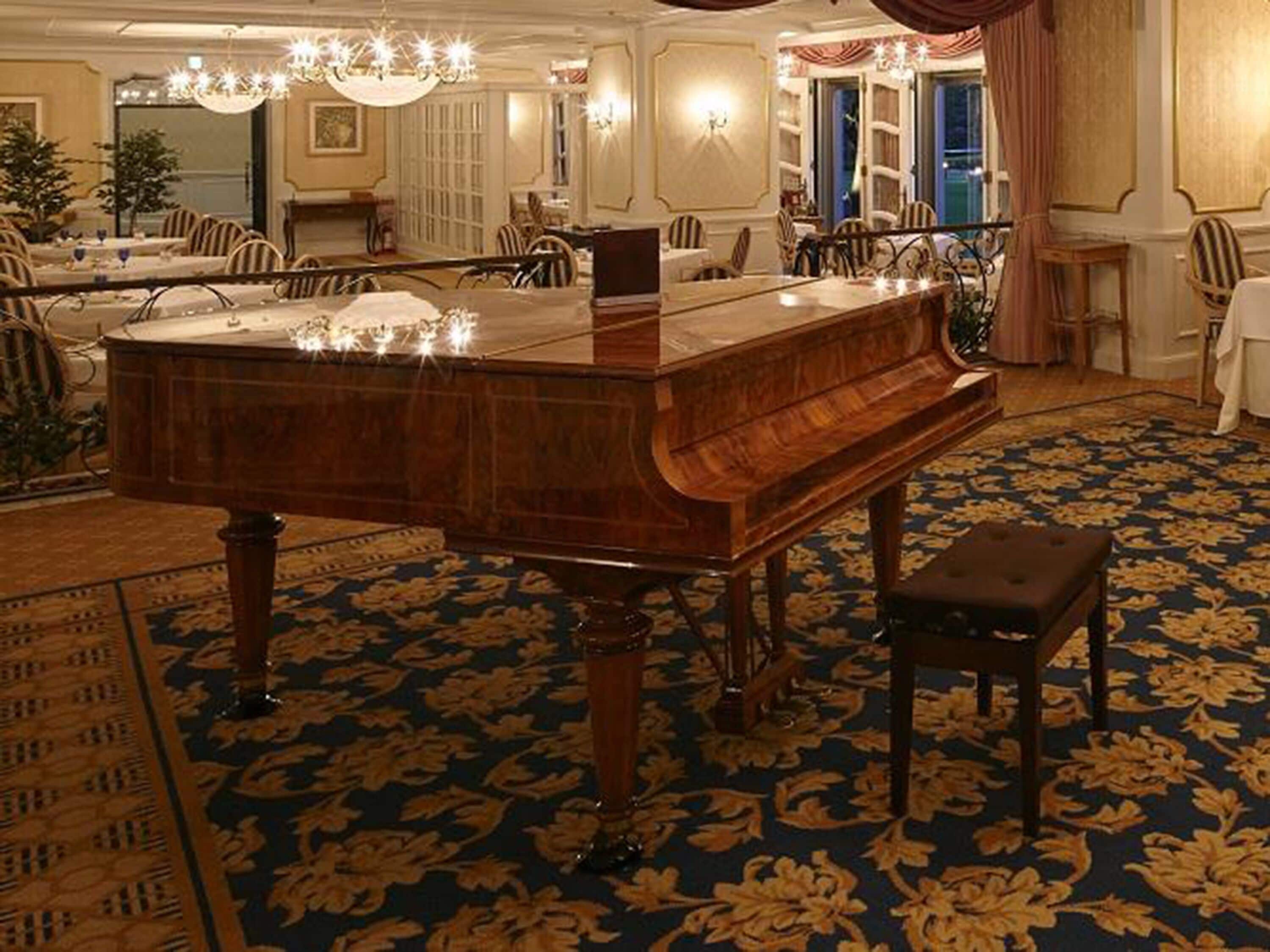 Un piano à queue dans une pièce spacieuse, agrémentée d’un tapis à motifs, de lustres élégants et d’un coin repas aménagé avec soin.