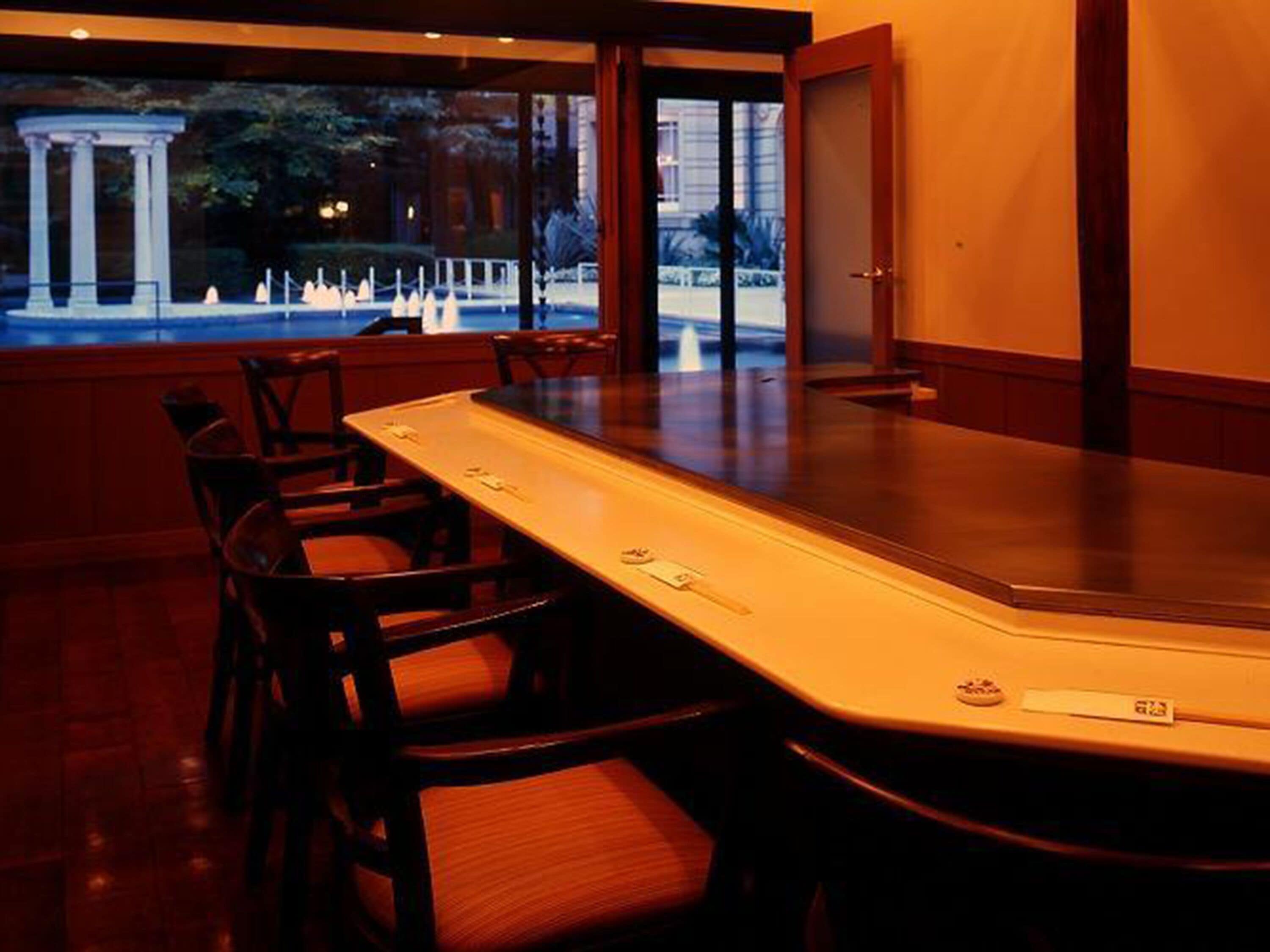 A conference room with a long table, chairs, and a view of a fountain outside.