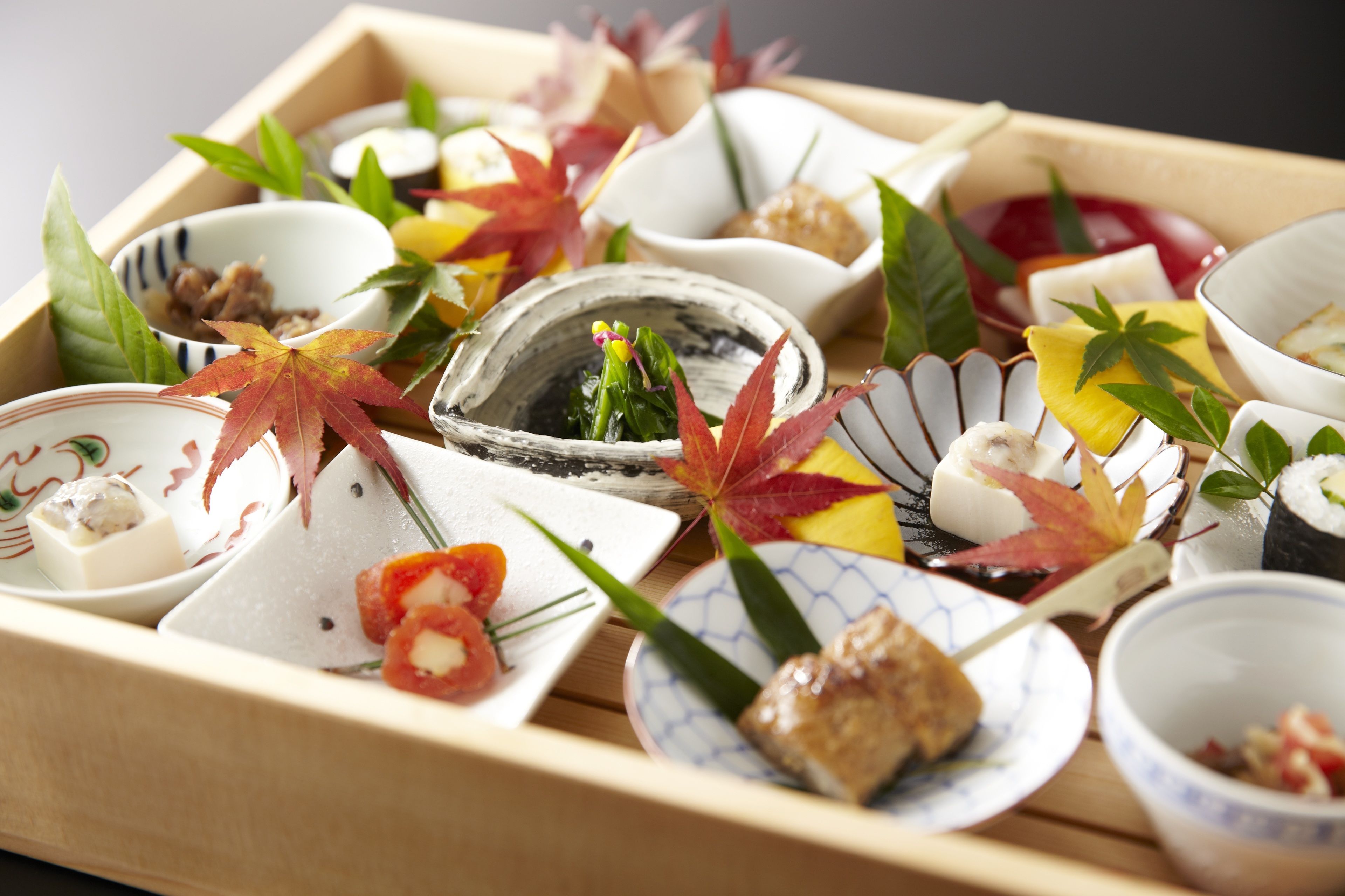 Un plateau en bois contenant divers petits plats, dont certains sont décorés de feuilles et d’autres éléments ornementaux.