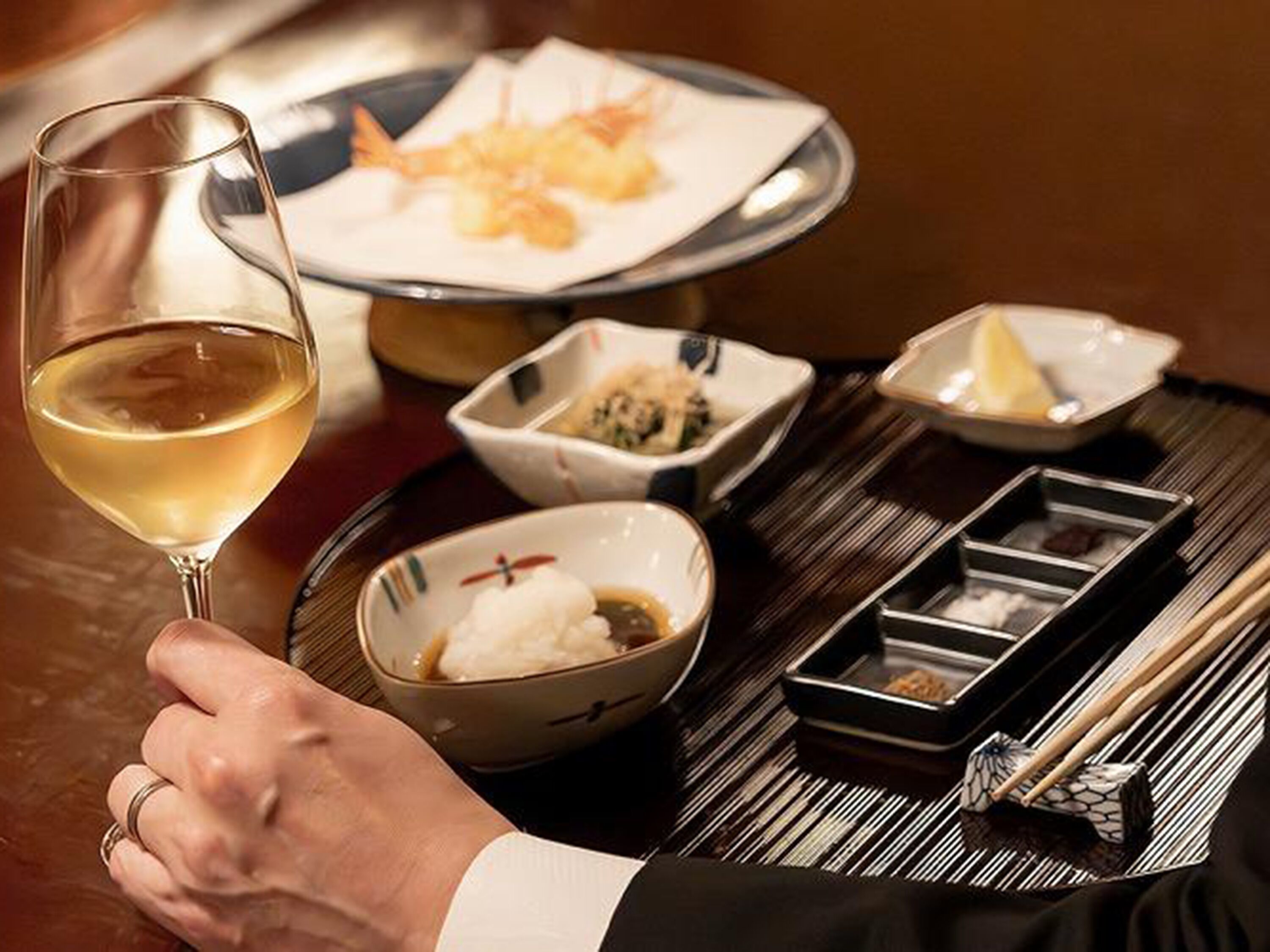 A dining table with a glass of white wine, a plate of food, and several small dishes with condiments.