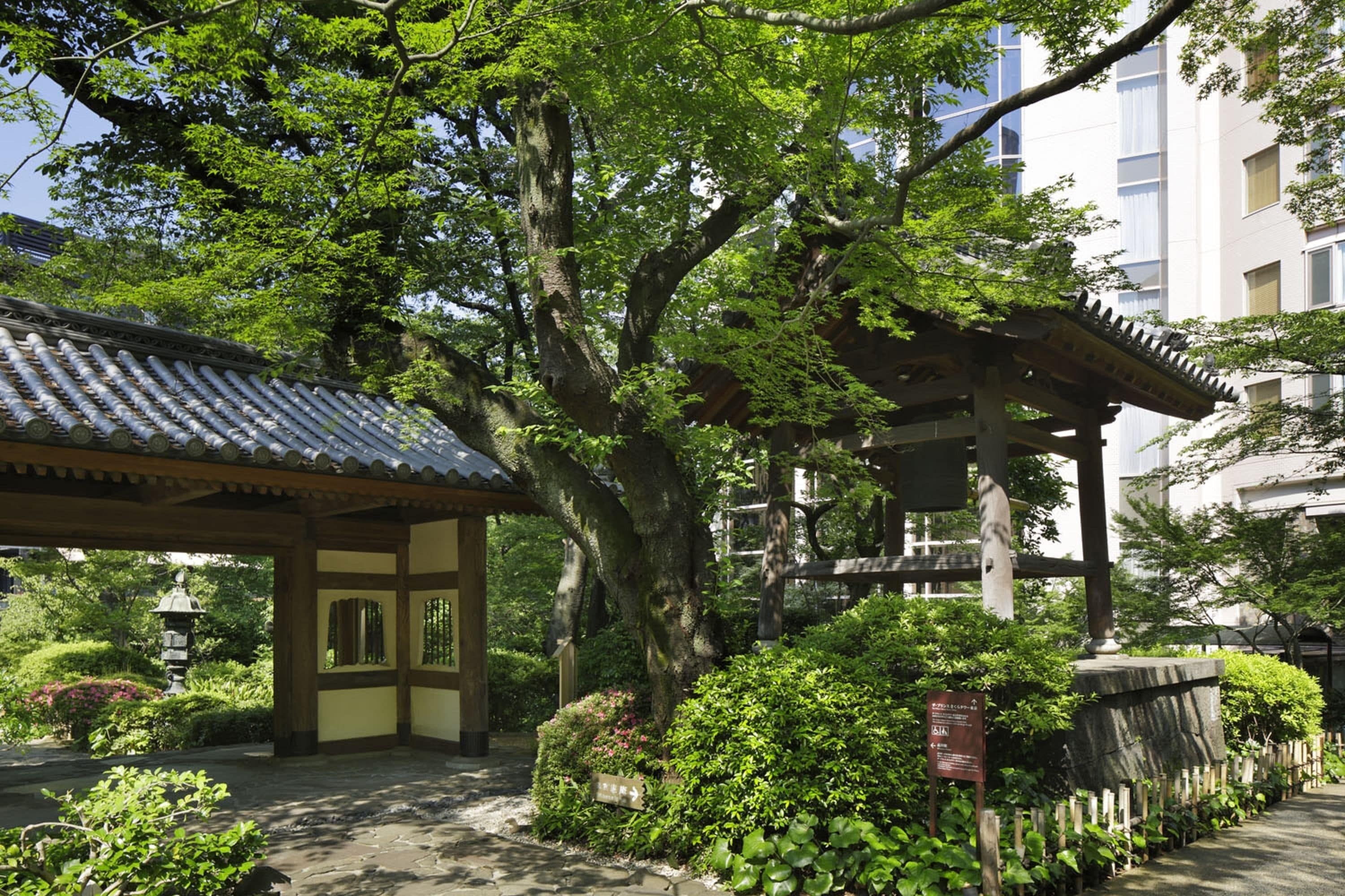 A traditional Japanese garden with a wooden pavilion, stone lantern, and lush greenery.