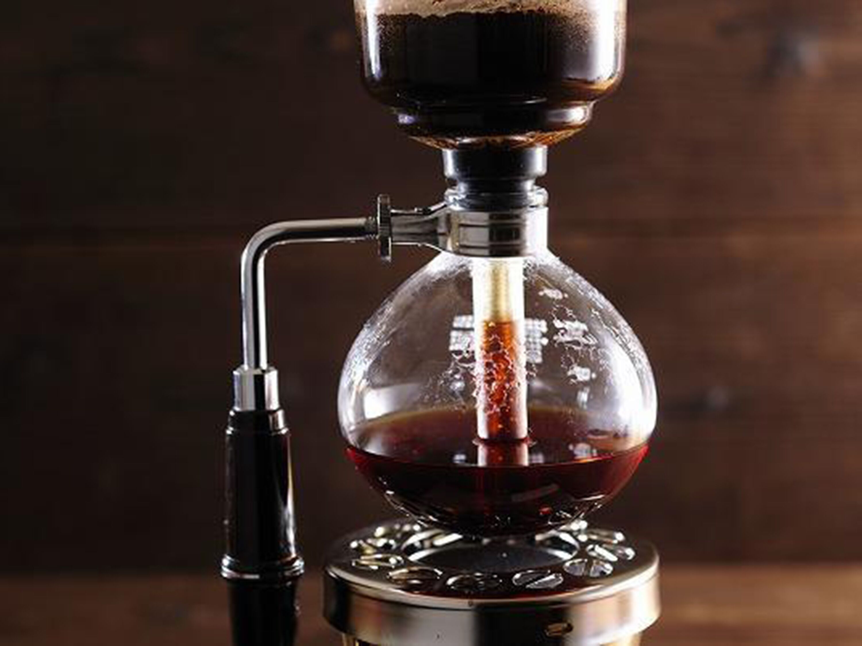 A coffee brewing device with a clear glass container and a metal base.