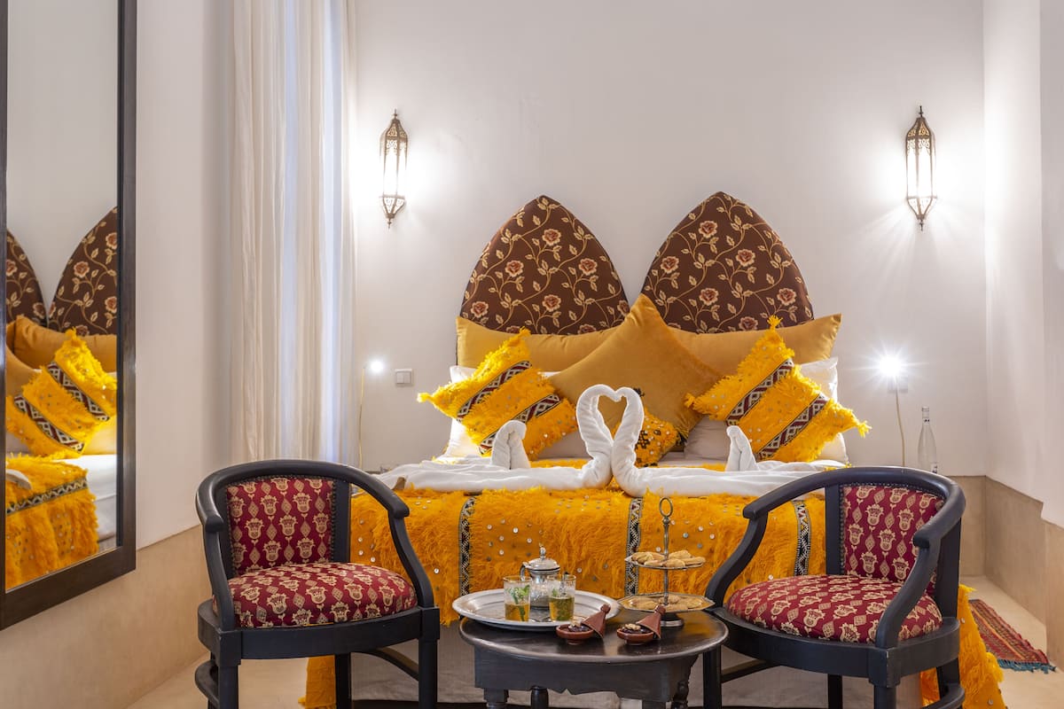 A hotel room with a bed, two armchairs, a small table with a tray of food, and wall-mounted lights.