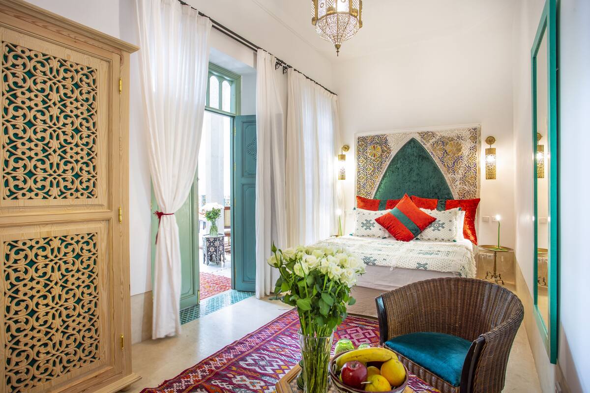 A bedroom with a bed, a chair, a table with fruit, and a vase of flowers.