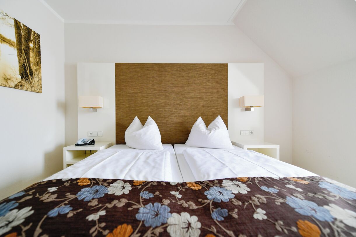 A hotel room with a bed, two bedside tables, a wooden headboard, and a floral bedspread.