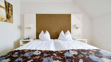 A hotel room with a bed, two bedside tables, a wooden headboard, and a floral bedspread.