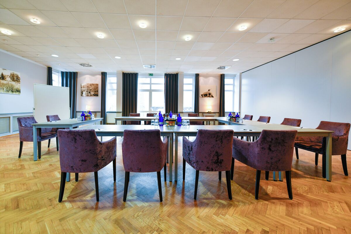 Ein Konferenzraum mit einem langen Tisch, violetten Stühlen und einer Tafel.