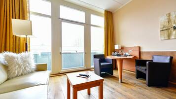 A hotel room with a sofa, a small table, two chairs, a desk, and a large window with curtains.