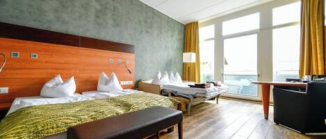 A hotel room with a large bed, a smaller bed, a desk, and a view of the city through large windows.