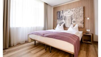 Un dormitorio moderno con una cama grande, suelo de madera, un ventanal con cortinas traslúcidas y una obra de arte colgada en la pared.