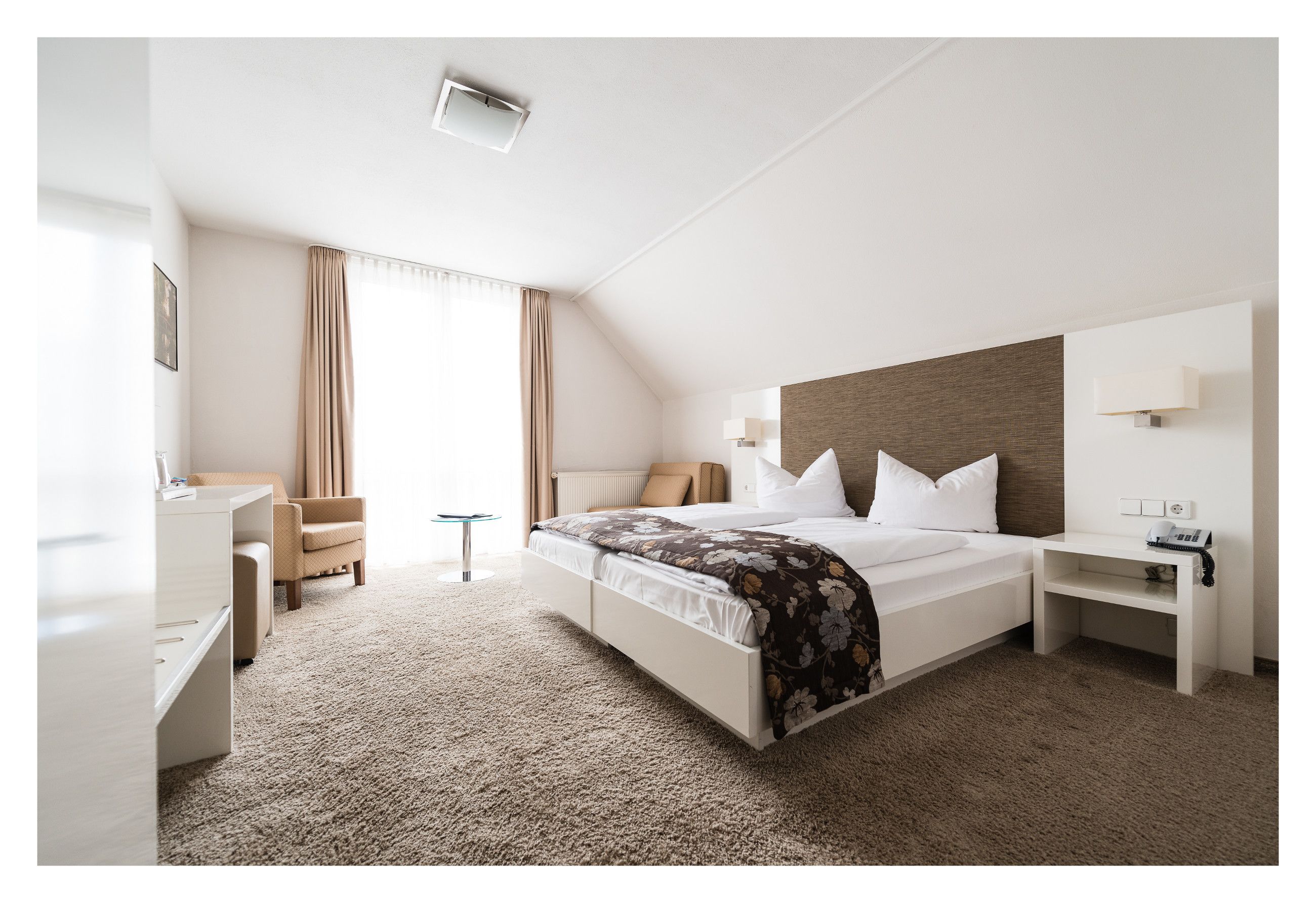 Una habitación de hotel con cama, mesita de noche, lámpara, silla y escritorio con otra silla.