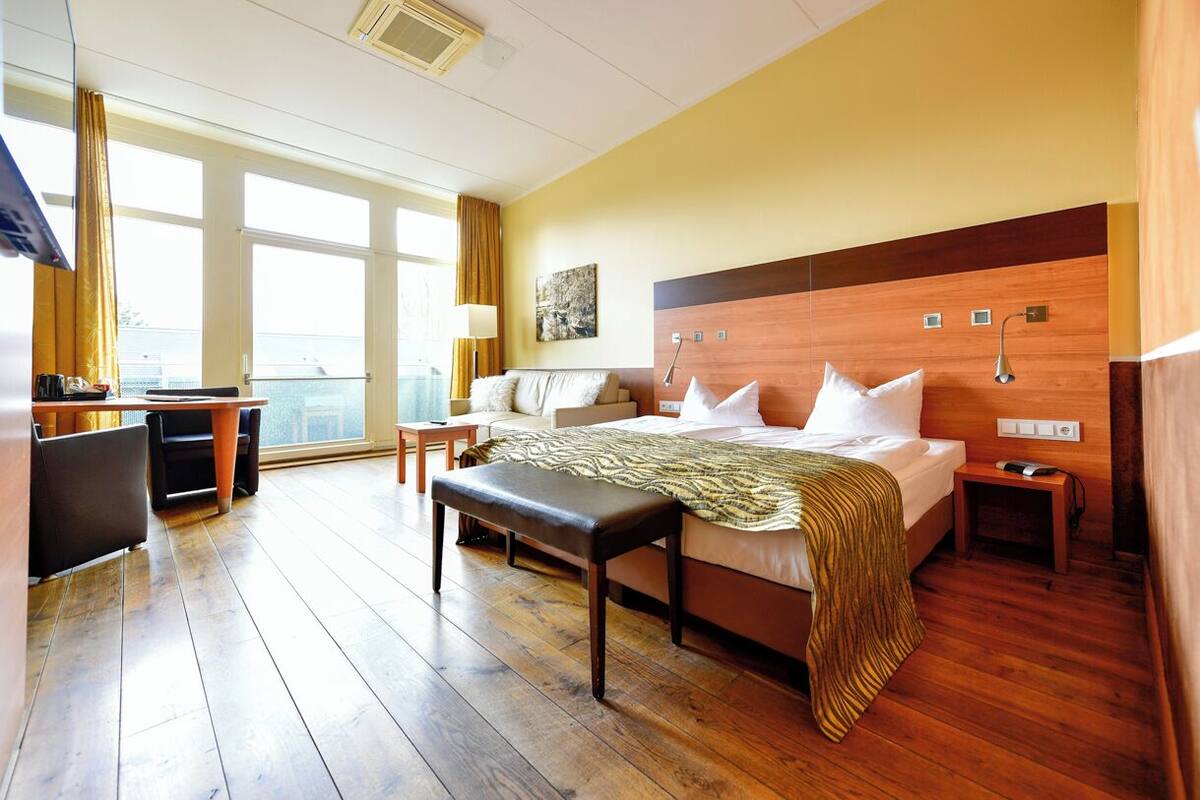 A hotel room with a large bed, a desk, a chair, and a window with curtains.