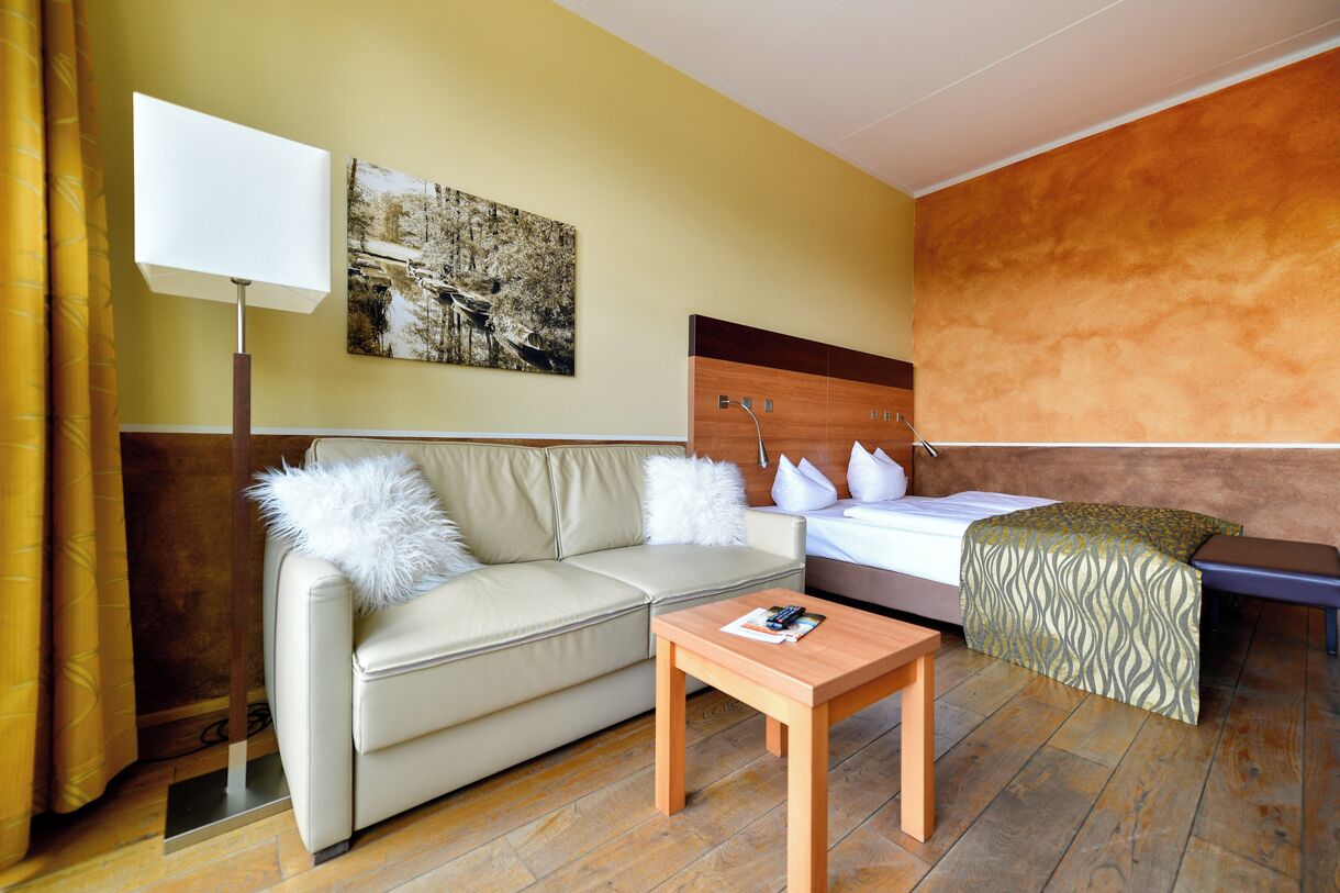 Una camera d'albergo con un letto, un divano, un tavolo, una lampada e un quadro appeso al muro.