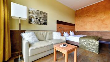 Una camera d'albergo con un letto, un divano, un tavolo, una lampada e un quadro appeso al muro.