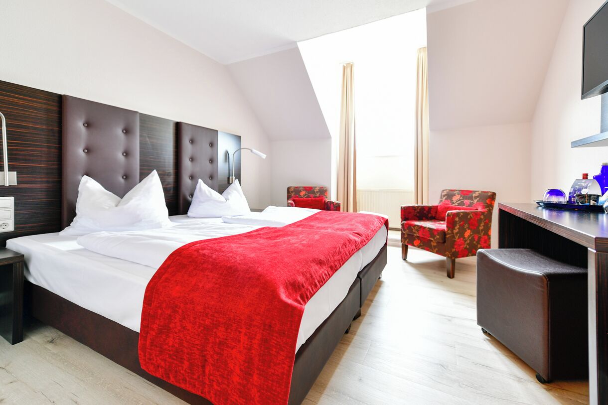 Ein Hotelzimmer mit einem großen Bett, einem Schreibtisch, einem Sessel und einem Fernseher.