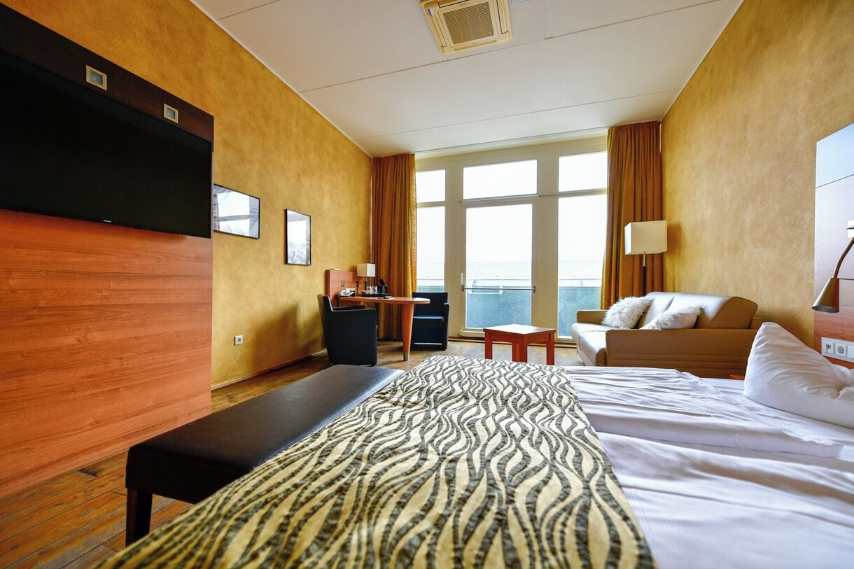 A hotel room with a large bed, a desk, a sofa, and a view of the sea.