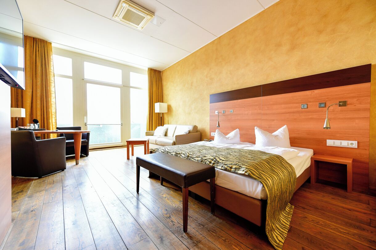 A hotel room with a large bed, a desk, a sofa, and a view of the city.