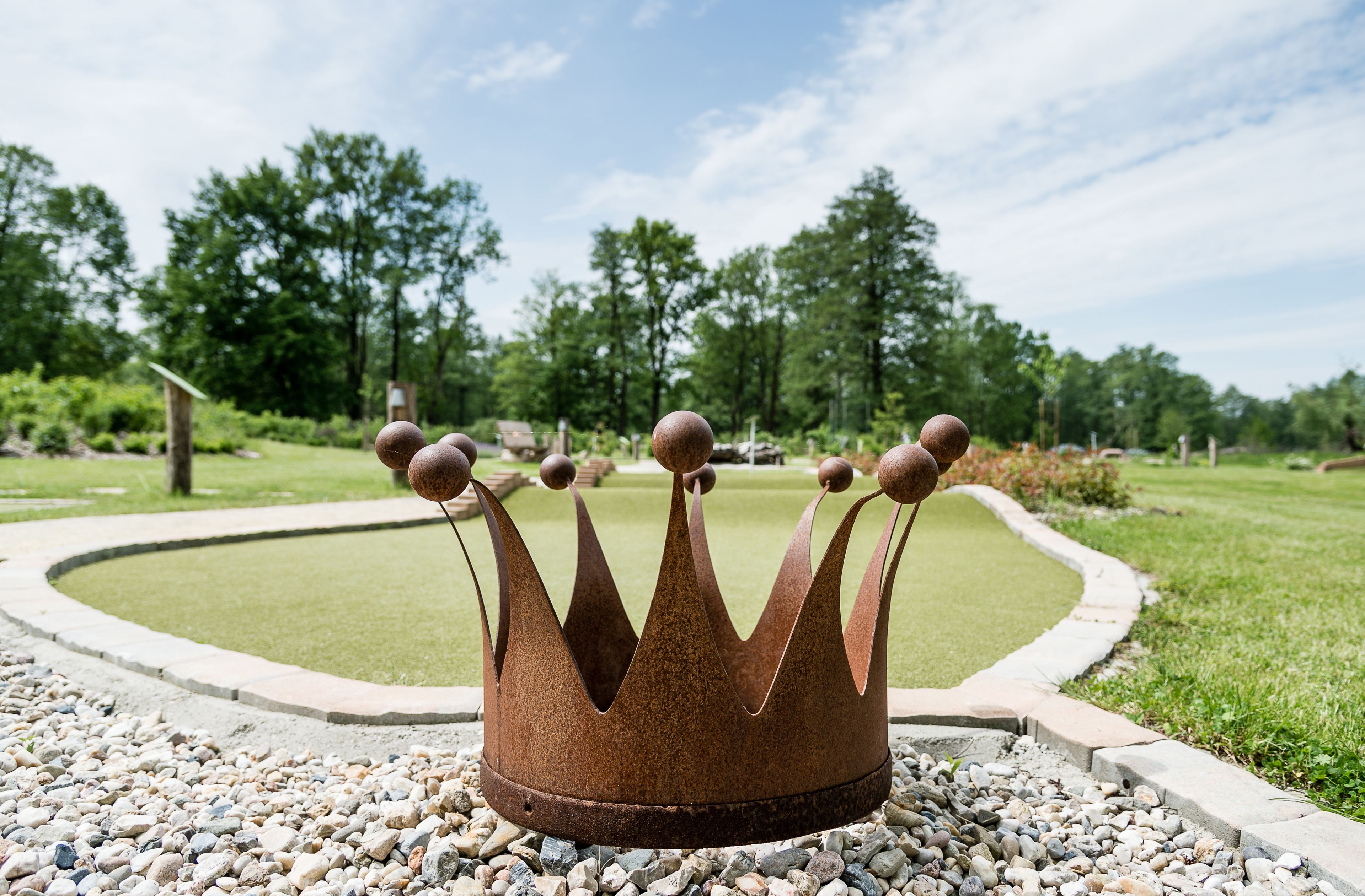 Una estructura en forma de corona de metal en un jardín ajardinado, con un sendero circular y abundante vegetación.