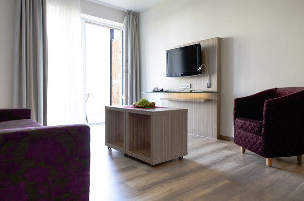 A modern living room with a flat-screen TV mounted on the wall, a wooden cabinet with a glass top, and a purple armchair. - Landhotel Burg Im Spreewald (Burg (Spreewald))