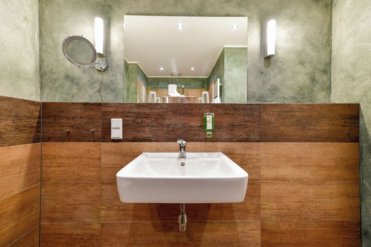 A bathroom with a white sink, wooden paneling, and a mirror with a round frame.