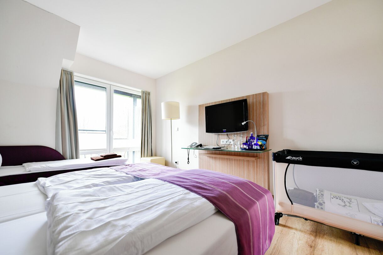 Een hotelkamer met twee bedden, een televisie, een bureau met een lamp en een raam met gordijnen.