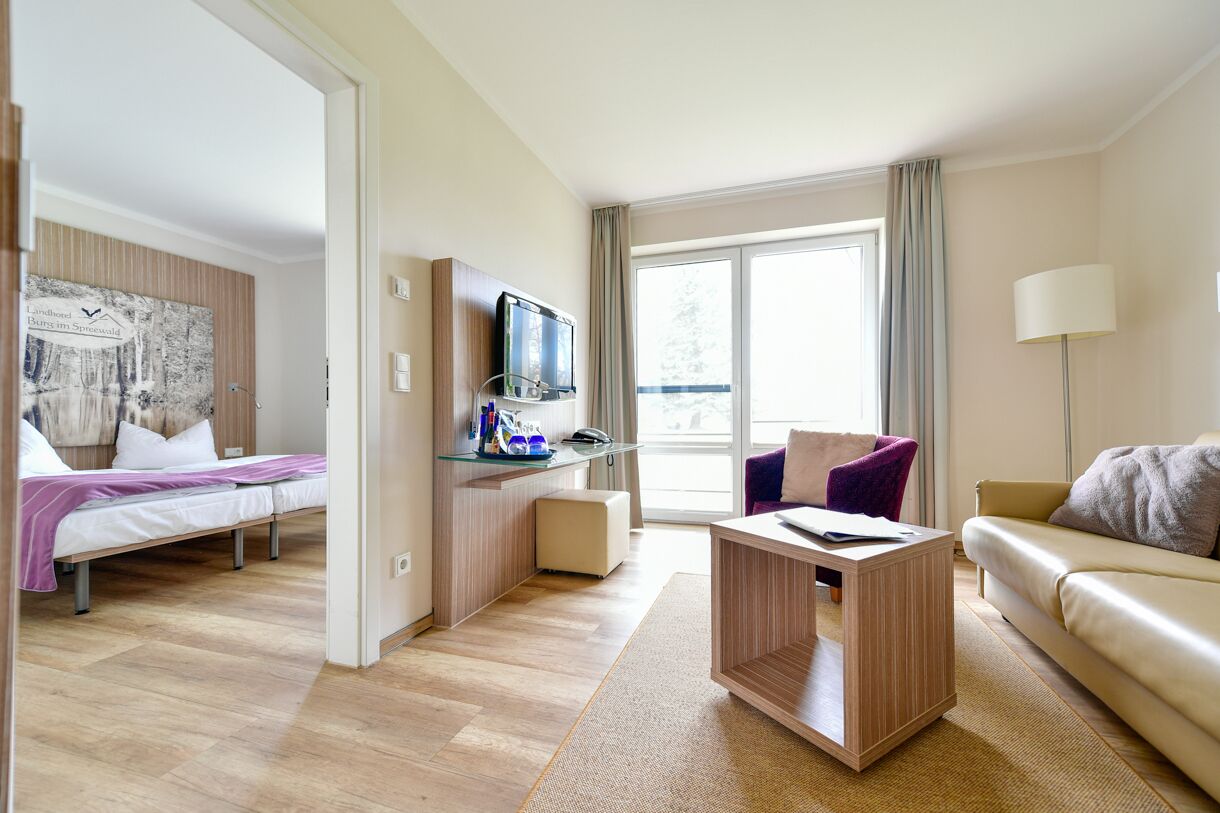 Et moderne hotelværelse med en seng, et skrivebord med computer, en sofa og et stort vindue.