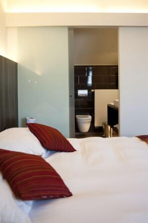 A hotel room with a bed, pillows, a nightstand, a bathroom with a toilet and sink. - Hotel Carpinus (Herent)