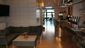 Un espace bar moderne avec un comptoir en marbre foncé, une variété de bouteilles et un coin salon comprenant un canapé et une table basse.