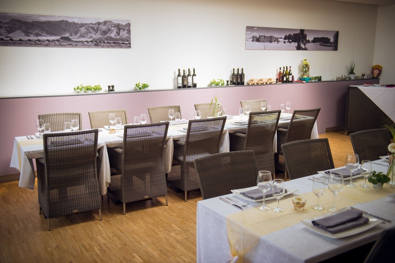 A dining area with tables set for four, wicker chairs, and a wall with two framed pictures.