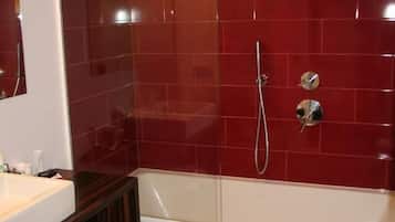 A modern bathroom with a red-tiled shower wall, a white bathtub, and a dark wooden vanity.