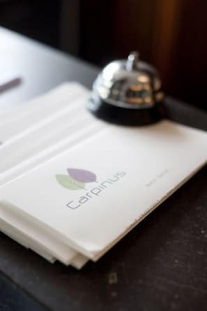A stack of white papers with a logo and text on the cover, placed on a dark surface. - Hotel Carpinus (Herent)