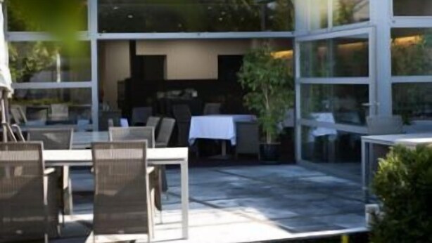 Un espace extérieur aménagé avec des tables et des chaises, un coin salon abrité et un bâtiment doté de grandes fenêtres.