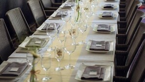 Une longue table à manger, entourée de nombreuses chaises, chacune agrémentée d’une serviette pliée et d’un verre.