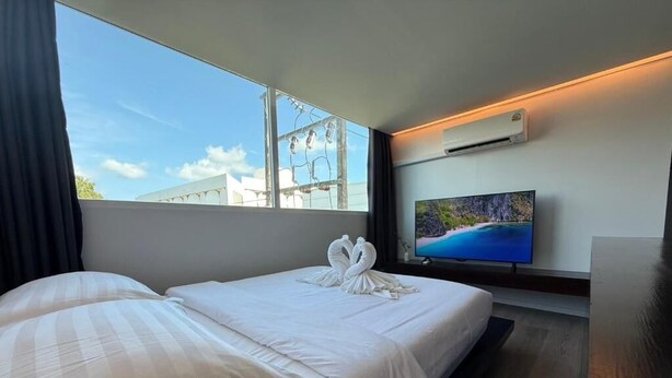 A hotel room with a bed, a TV, and a window with a view of buildings. - P168 Hostel Samui (Koh Samui)