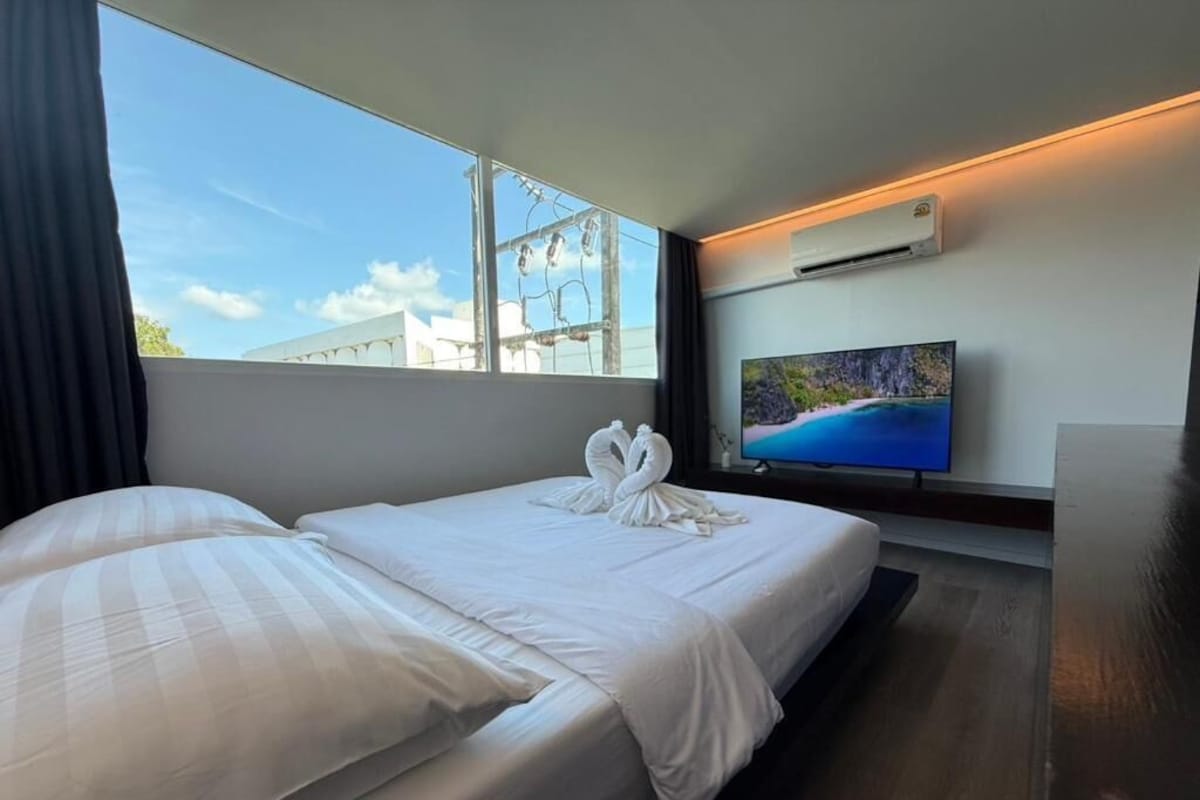 Una habitación de hotel con cama, televisión y ventana con vistas a edificios.