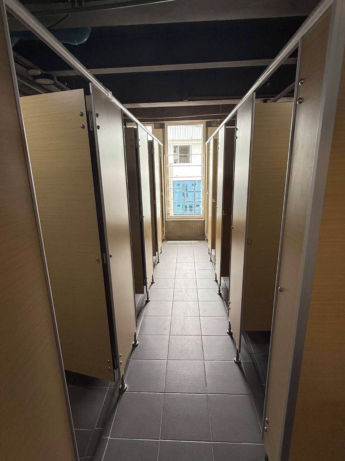 A corridor with multiple stalls, each with a door and a tiled floor.