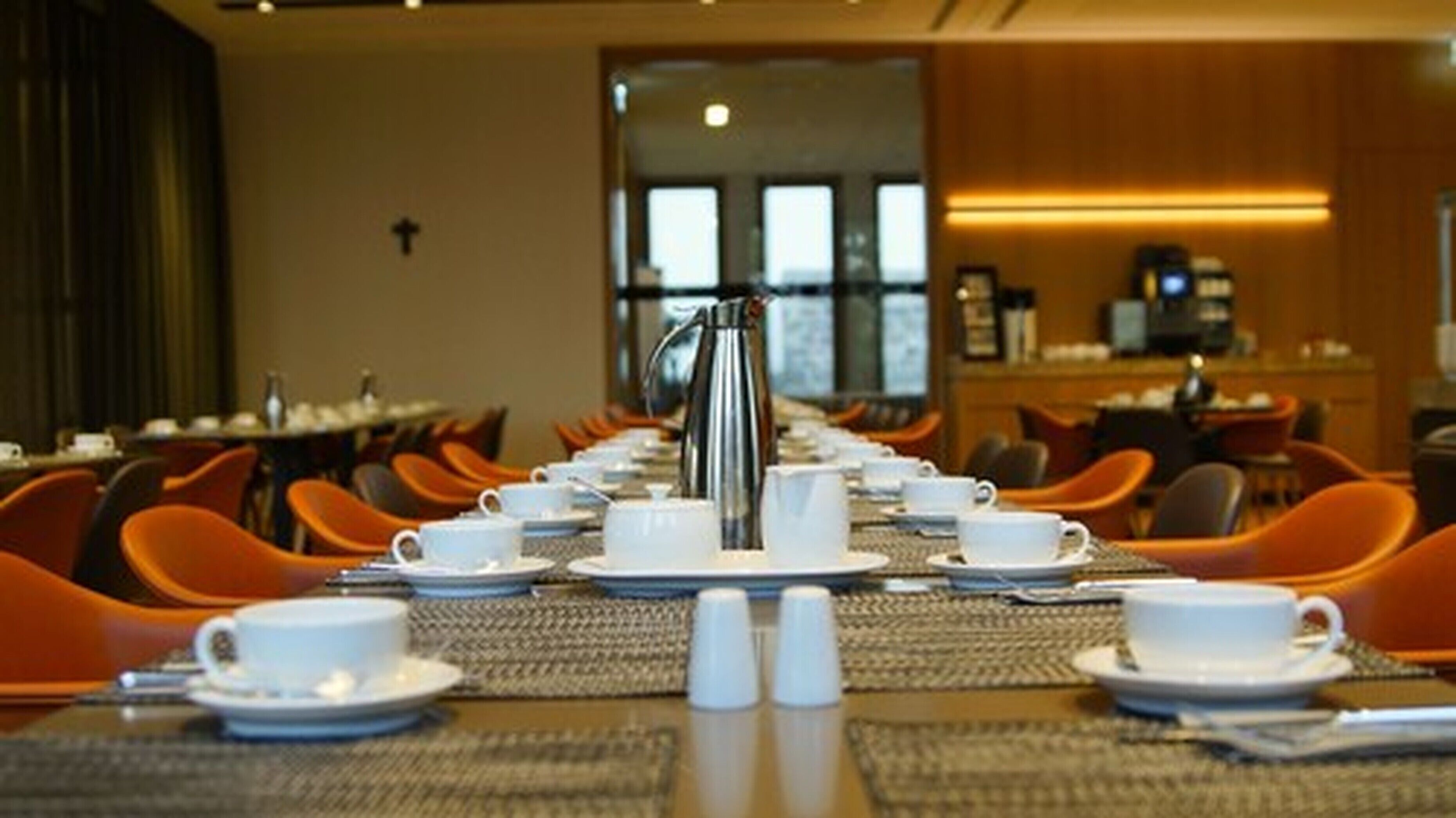 A breakfast setup with multiple tables, orange chairs, and a coffee station.