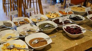 Buffet com diversos alimentos em tigelas, cada um identificado com seu nome.