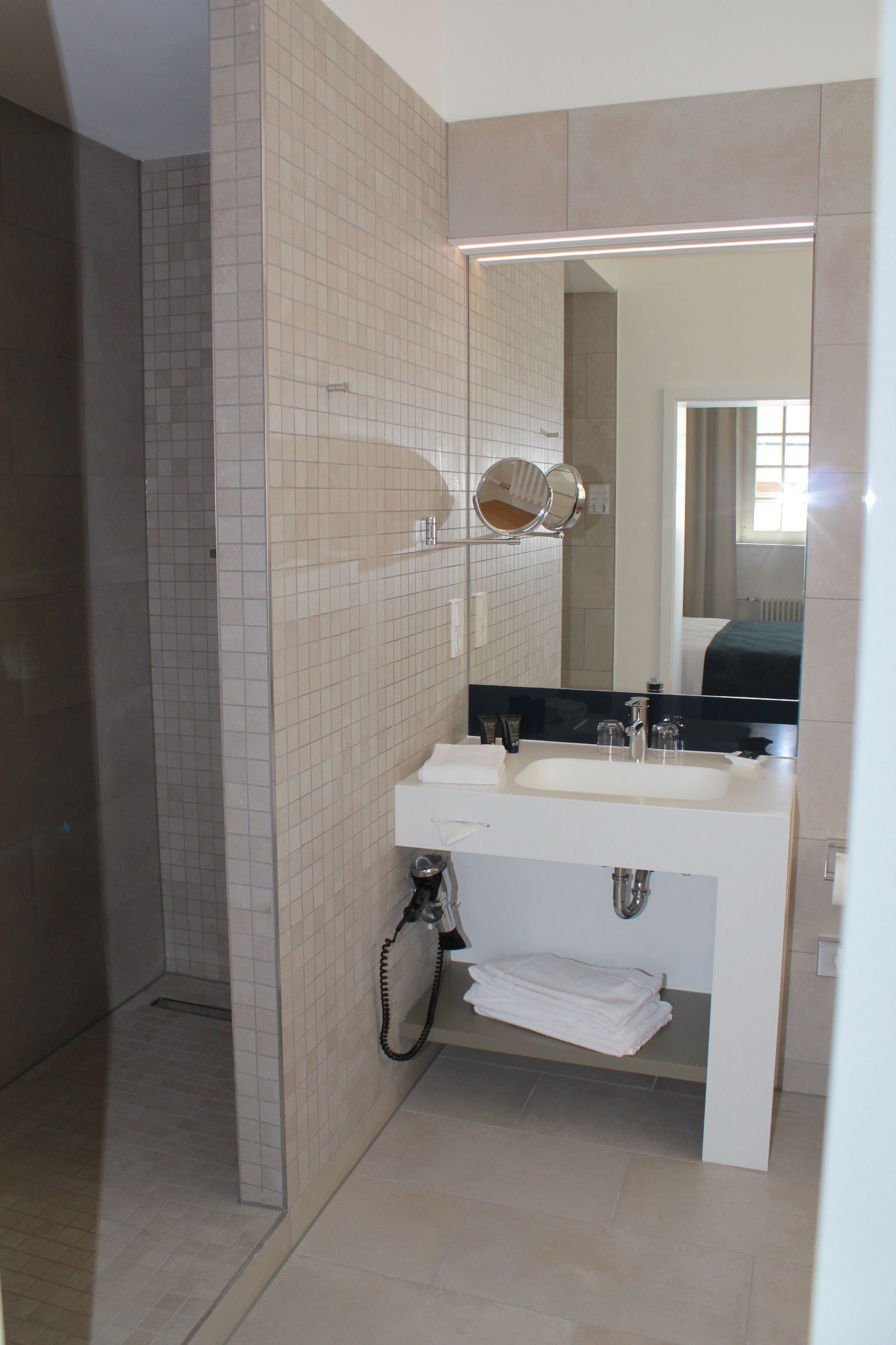 Un baño con lavamanos blanco, espejo y paredes de azulejos.