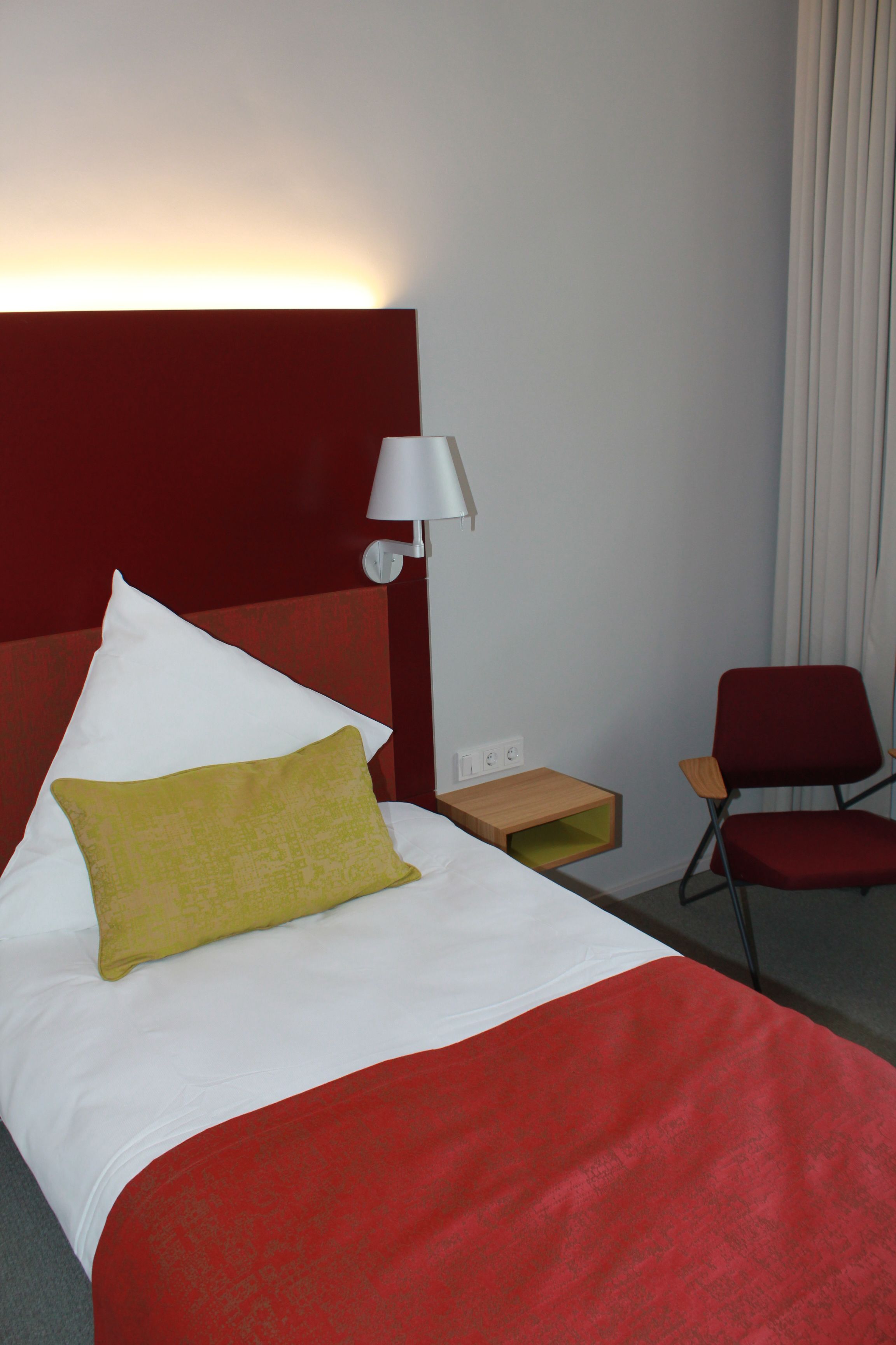 Una camera d'albergo con un letto, un comodino, una lampada e una sedia.
