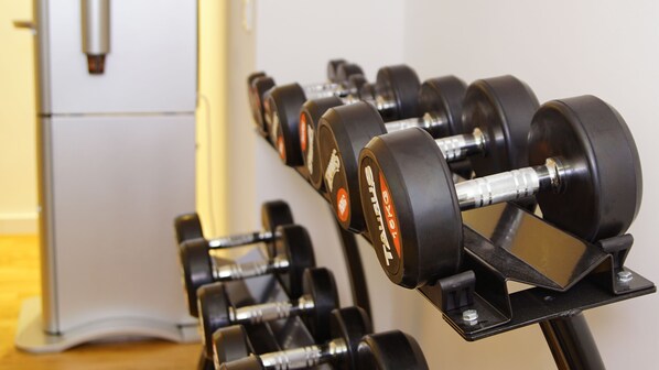 A row of black dumbbells on a rack with a white cabinet in the background. - Katholisch-Soziales Institut (Siegburg)