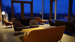 A modern lounge area with multiple seating options, large windows offering a view of the cityscape, and ambient lighting.