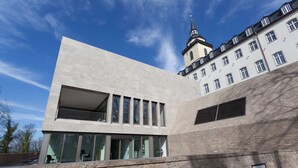 A modern building with a large glass facade and a traditional building with a tower in the background.