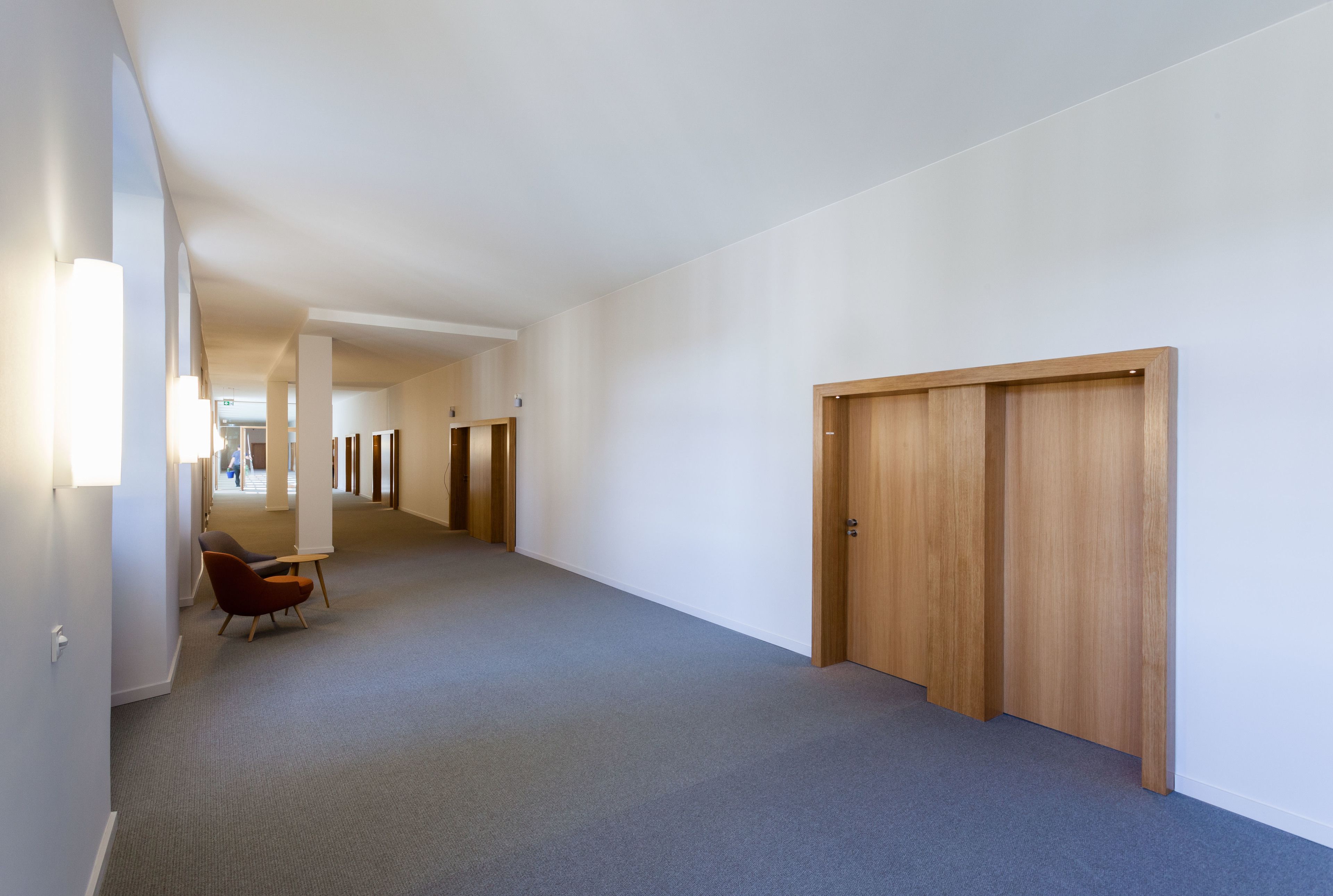 A hallway with a carpeted floor, wooden doors, and a chair.