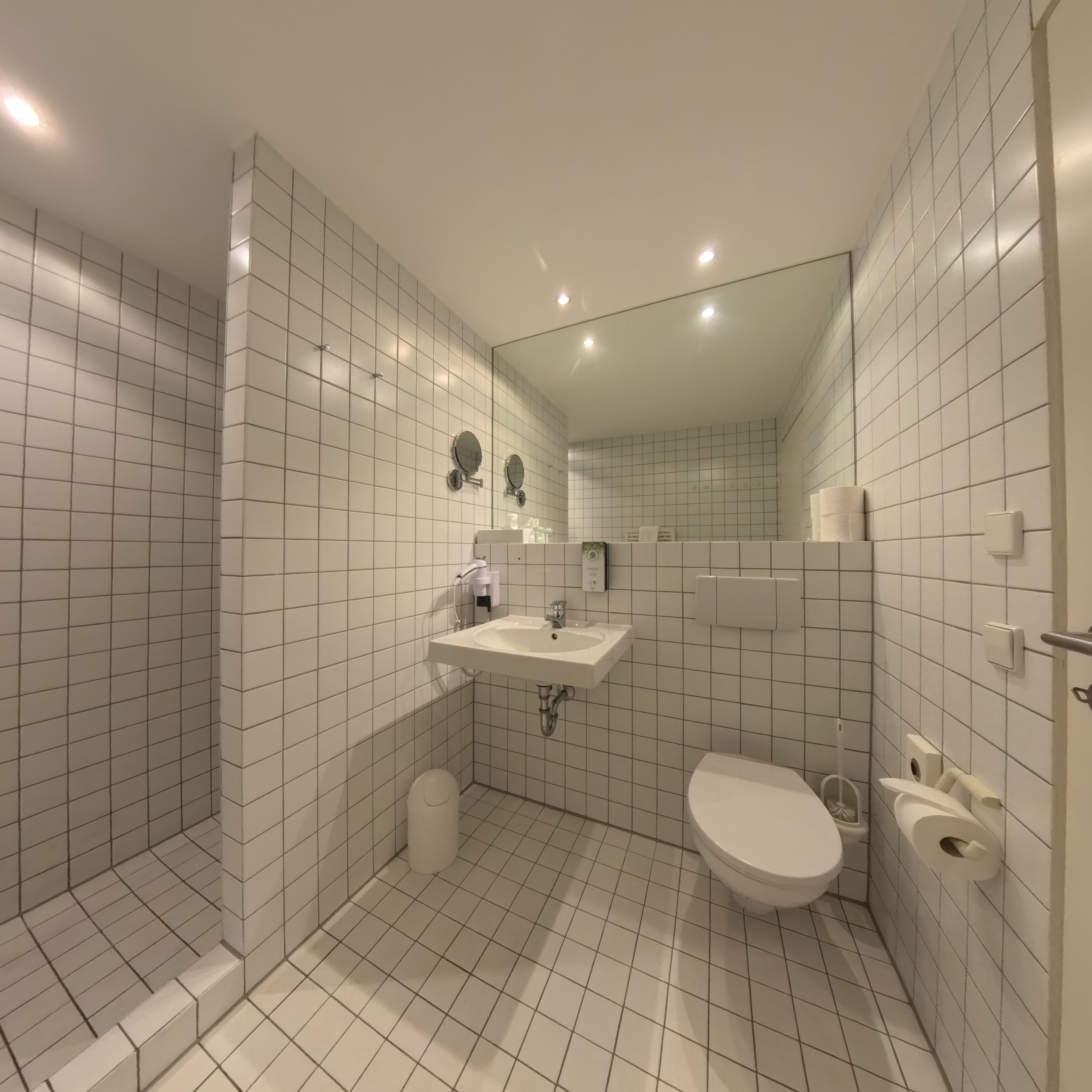 A modern bathroom with white tiles, a sink, a toilet, and a shower area.