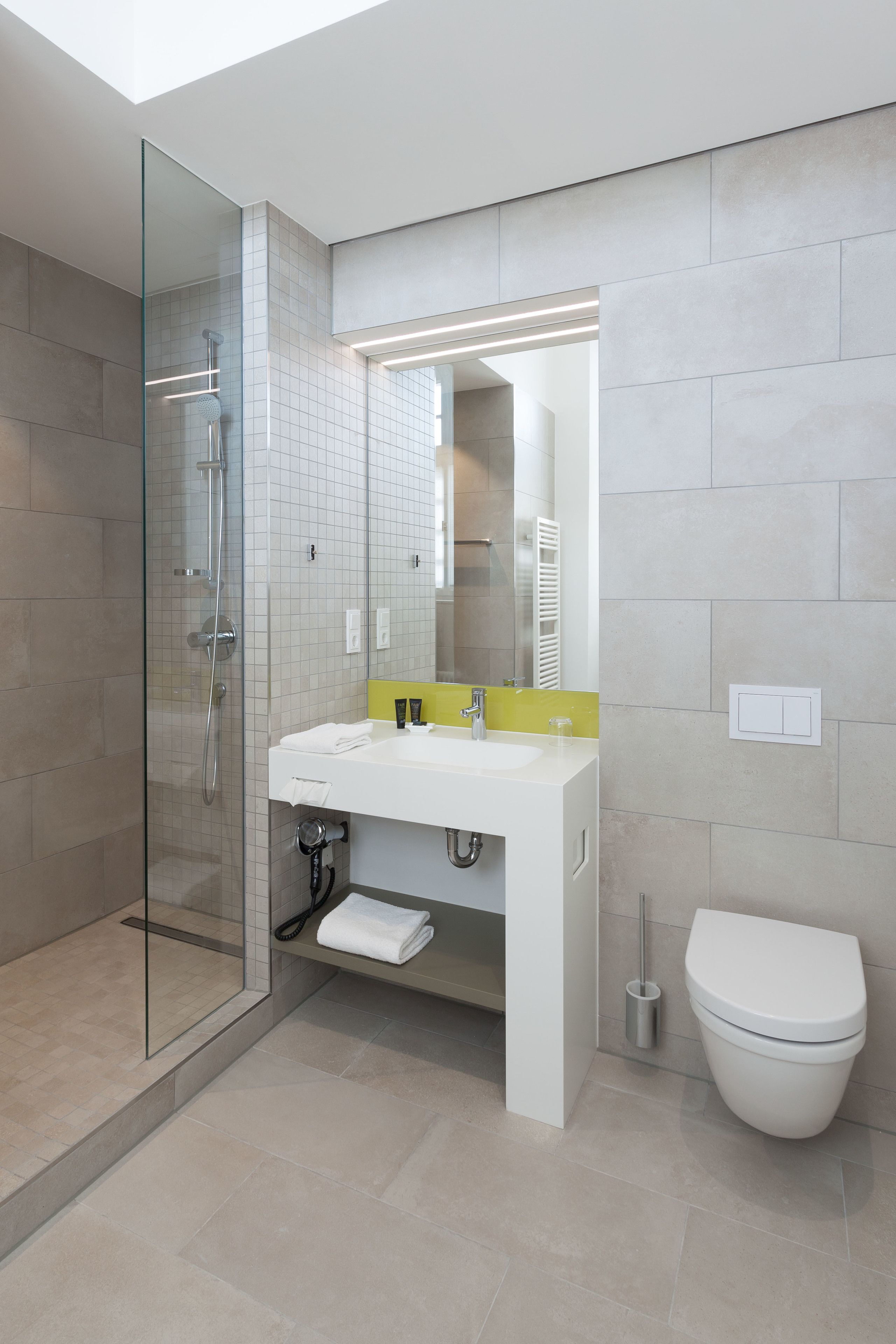 A modern bathroom with a glass shower enclosure, a white sink with a yellow accent, and a white toilet.