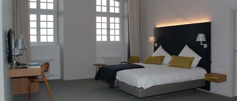 Un dormitorio con una cama, un escritorio, una silla y dos ventanas.