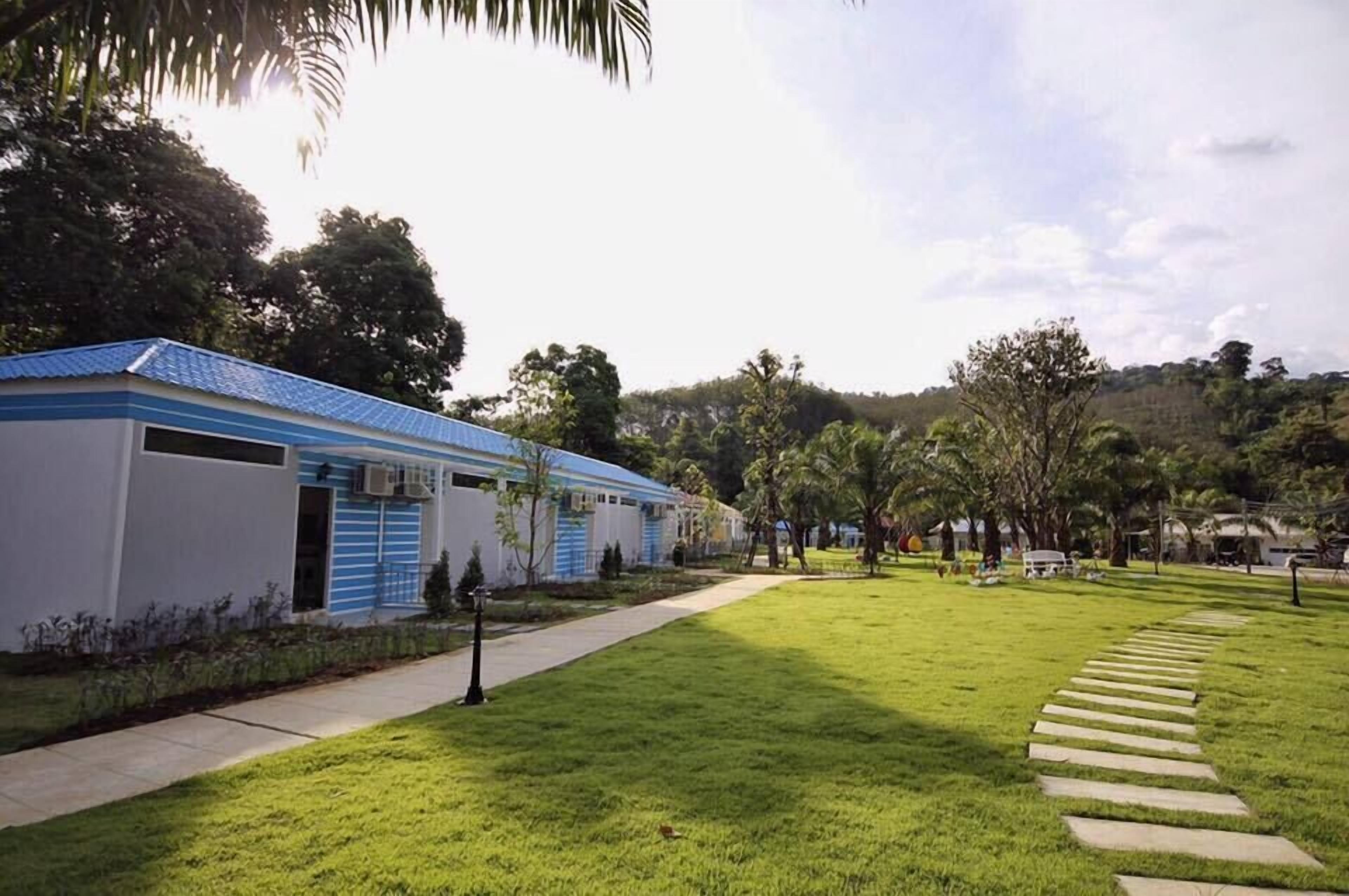 Zona residencial con hilera de casas, césped y un camino que lleva a un edificio con tejado azul.