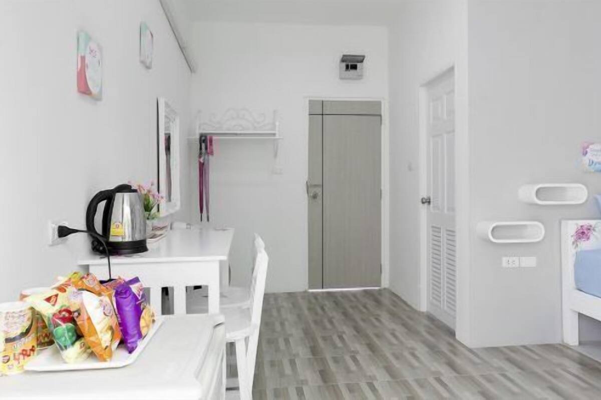 Un dormitorio con cama, mesita de noche y silla. Hay una pequeña mesa con aperitivos y una tetera.