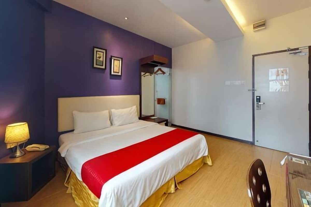 A hotel room with a bed, a nightstand, a lamp, a door, and a mirror.